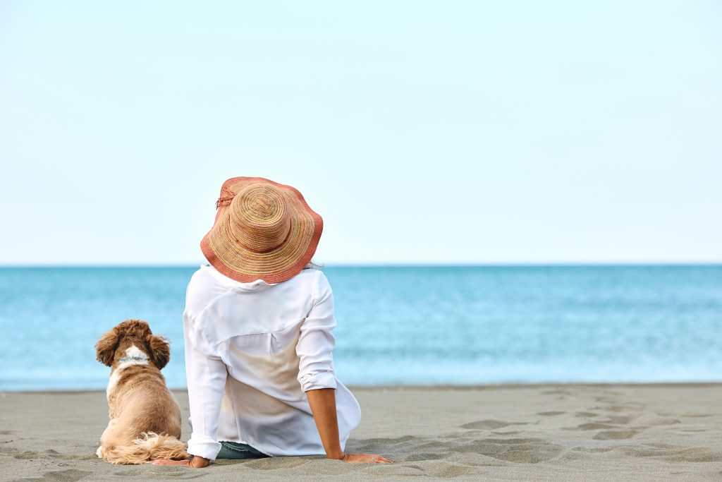 photo of the back of a woman on the beach with her dog.